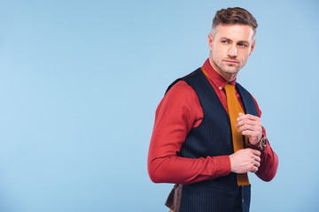 handsome stylish man in formal wear adjusting shirt isolated on blue with copy space