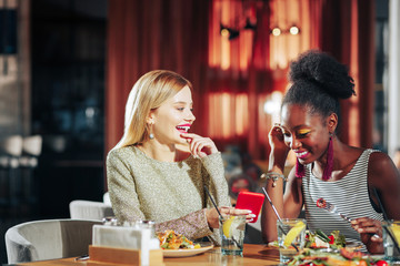 Blonde-haired woman showing photo of her boyfriend to her friend