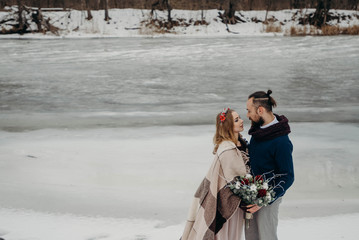 Winter wedding in forest. Romantic young couple together near river in destination forest on winter holiday, hugging being romantic, outdoors. Travel lifestyle, coastal exterior space.