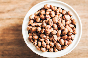 Beans (Phaseolus) in white porcelain bowl on wooden background, vegetarian concept.