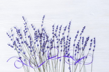 Obraz premium Lavender flowers and ribbon on white wooden background withcopy space. Branches of lavender on wood.