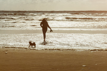 Woman and her dog walking at the beach at sunset or sunrise