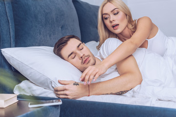 jealous woman reaching for smartphone while boyfriend sleeping in bed, mistrust concept