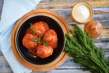 Meatballs with sauce and greens in a pan on a wooden background.