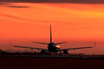 Naklejka na ściany i meble 真っ赤な夕焼けから離陸する航空機　　Aircraft to take off from a bright red sunset　　The most beautiful Radiates the glow of the sunset Flying happiness Aircraft image carrying good luck