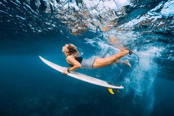 Attractive surfer woman with surfboard dive underwater with under wave.