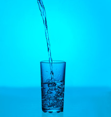 Splashes of water. Glass of cold water on a blue background. 
