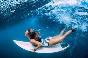 Surfer girl with surfboard dive underwater with fun under ocean wave.