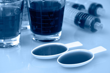 Medicinal cup, oral syring and teaspoon filled with oral syrup medicine.