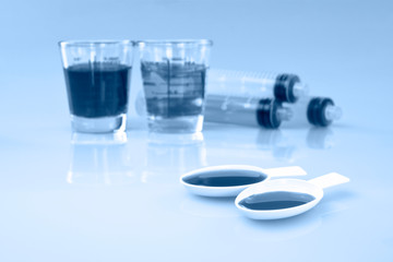 Medicinal cup, oral syring and teaspoon filled with oral syrup medicine.