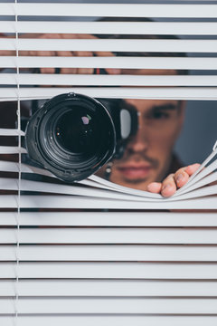 close-up view of young man holding camera and looking at camera through blinds