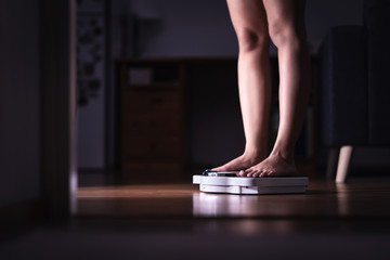 Weight loss and diet concept. Lady standing on scale. Woman weighing herself. Fitness lady dieting. Weightloss and dietetics. Dark late night mood. - obrazy, fototapety, plakaty
