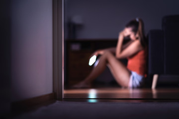 Sad teenager with smartphone in her room sitting on floor. Lonely teen girl crying with mobile...