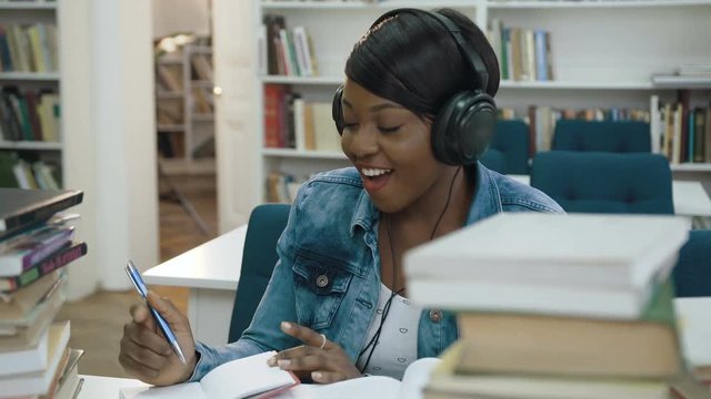 Atractive african young woman listening music in the headphone while making some note from note book for university.