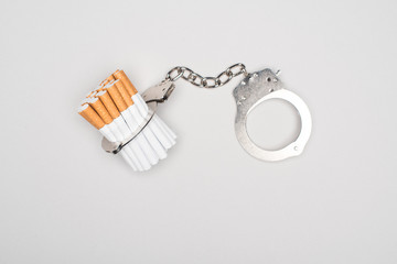 Studio shot of handcuffs and cigarettes isolated on grey, nicotine addiction concept