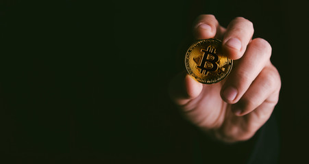 Closeup of golden bitcoin BTC cryptocurrency in hand over dark black background.