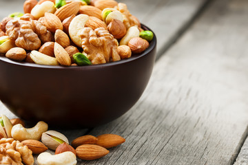 Wooden bowl with mixed nuts on a wooden gray background. Walnut, pistachios, almonds, hazelnuts and cashews, walnut.