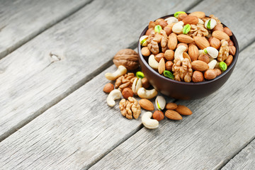 Wooden bowl with mixed nuts on a wooden gray background. Walnut, pistachios, almonds, hazelnuts and cashews, walnut.