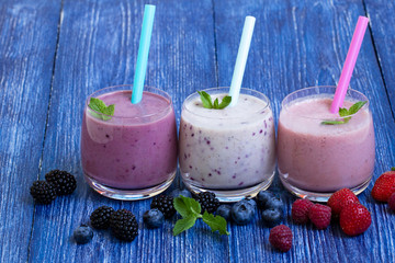 Raspberry, strawberry and blueberry smoothie on blue wooden background. milkshake with fresh berries. berry yogurt with blueberries, raspberries and blackberries. summer vegetarian Breakfast.