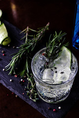 Gin-tonic alcoholic cocktail. Cucumber, rosemary, ice. On a black wooden background.