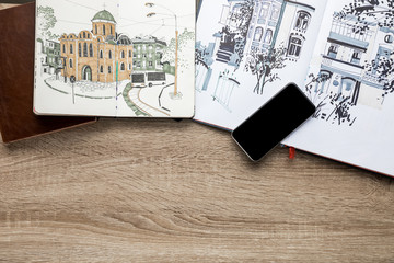 Fototapeta na wymiar top view of drawings in albums and smartphone on wooden background