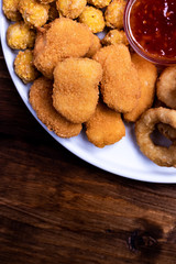 Snacks for beer on a white plate are: chicken nuggets, onion rings in tempura, chicken popcorn and chili sauce