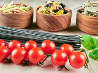 Fototapeta na wymiar Dried pasta: colorful orechiette, fusilli , tagliatelle, spaghetti, fresh tomatoes and basil, on a wooden board