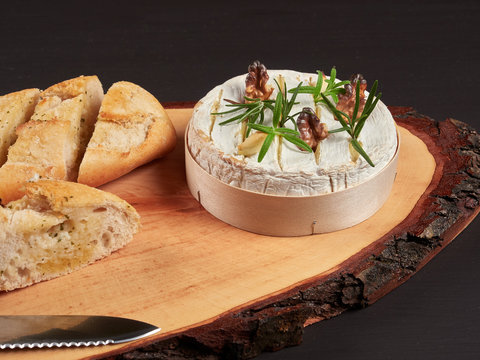Baked Camembert with walnuts, rosemary stalks and garlic cloves, served with crusty garlic gread, on a rustic board