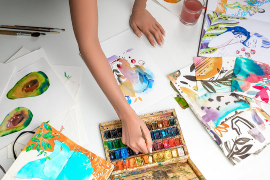 selective focus of female hands mixing watercolor paints surrounded by color pictures