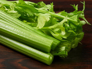 Fresh green celery stalks on a dark rustic wooden oak board
