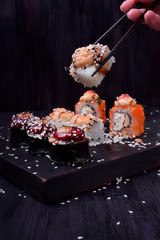 Female hand is holding a sushi roll with chopsticks