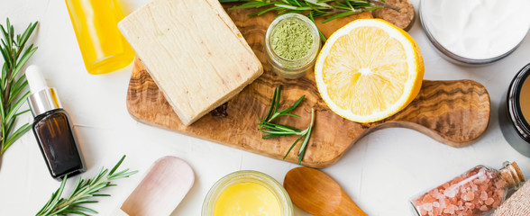 Spa still life with organic ingredients , top view of natural soap, clay, essential oil, rosemary herb, lemon and bath salt on wooden board, organic ingredient for skincare treatments