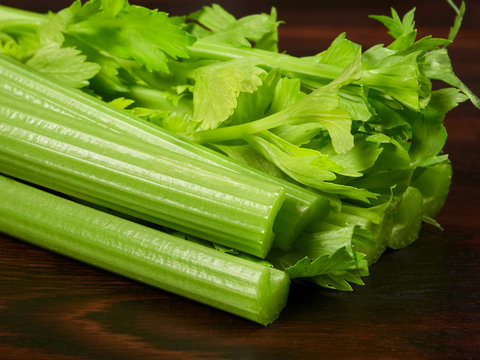 Fresh green celery stalks on a dark rustic wooden oak board