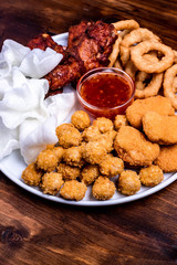 Beer snacks on the plate: chicken nuggets, onion rings in tempura, chicken popcorn, rice chips, fried chicken pieces and ketchup