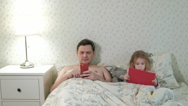 dad and little daughter on the bed playing on the tablet
