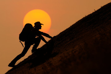 Silhouette of backpacker climbing on mountain at sunset or sunrise