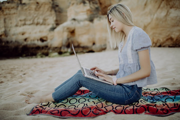 Freelance concept. Blonde young woman in casual clothes with a laptop sitting at the seaside