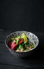 Pho Bo vietnamese soup with noodles, beef, chili pepper, onion,  cilantro and lime on dark black background with copy space on top
