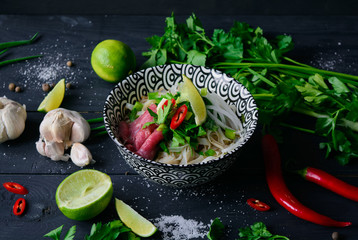 Pho Bo vietnamese soup with noodles, beef, chili pepper, onion,  cilantro and lime on dark black background