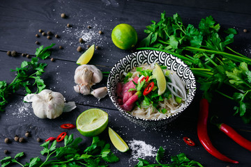 Pho Bo vietnamese soup with noodles, beef, chili pepper, onion,  cilantro and lime on dark black background