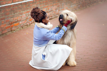 African girl in a coat playing with a dog of the Briard breed on a city street on a winter day close-up. - 245382433