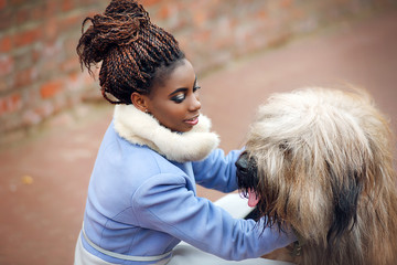 African girl in a coat playing with a dog of the Briard breed on a city street on a winter day close-up.