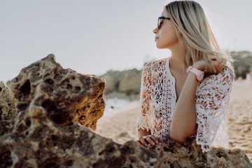 Fototapeta na wymiar Portrait of young beautiful woman in bikini and white coat sitting at rocks on the ocean beach
