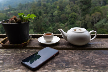 Tea with Tea pot and smart phone on wooden table in tea plantation