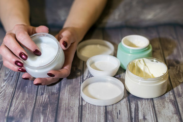 A young woman is holding a jar of cream. Manicure with red lacquer. On the table are open jars of cream. Salon skin care.