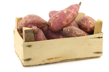 freshly harvested sweet potatoes in a wooden crate on a white background