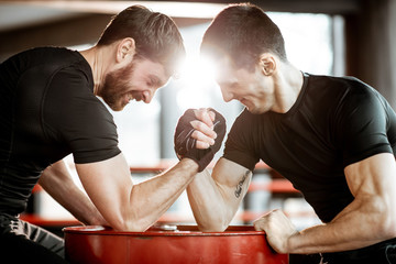 Two young athletes in black sportswear having a hard arm wrestling competition on a red barrel in the gym - obrazy, fototapety, plakaty