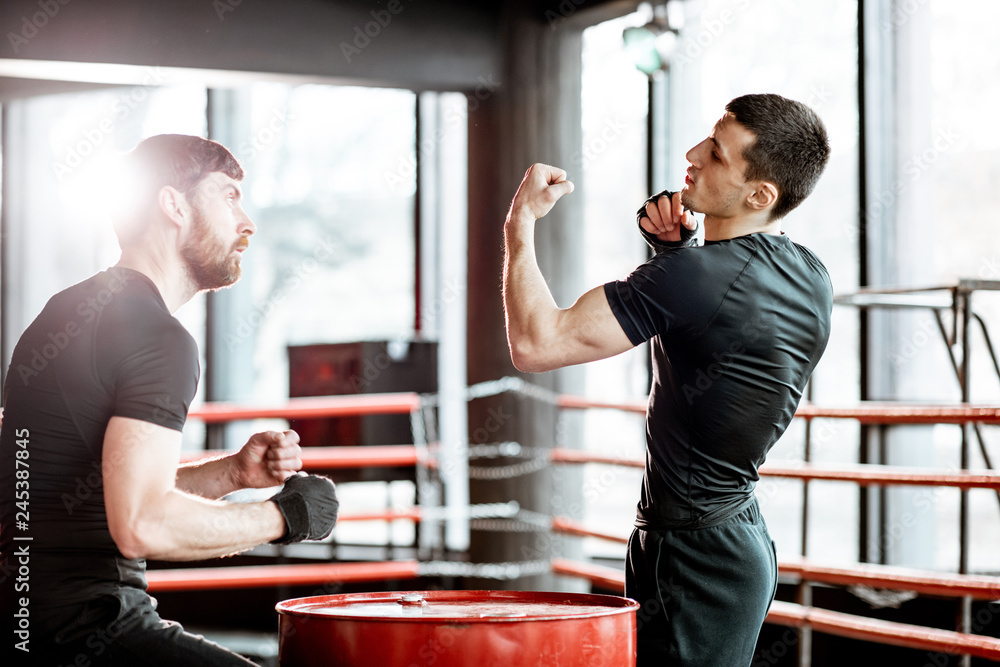 Wall mural Boxing trainer showing to a man how to fight, teaching to box in the boxing ring at the gym