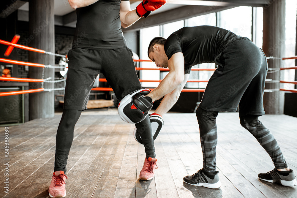 Wall mural Boxing trainer keeping leg of a man learning how to fight correctly on the boxing ring at the gym