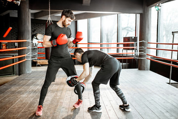 Fototapeta na wymiar Boxing trainer showing to a man how to fight, teaching to box on the boxing ring at the gym